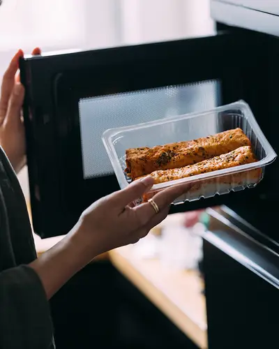 A woman places a plastic tray of food in a microwave.