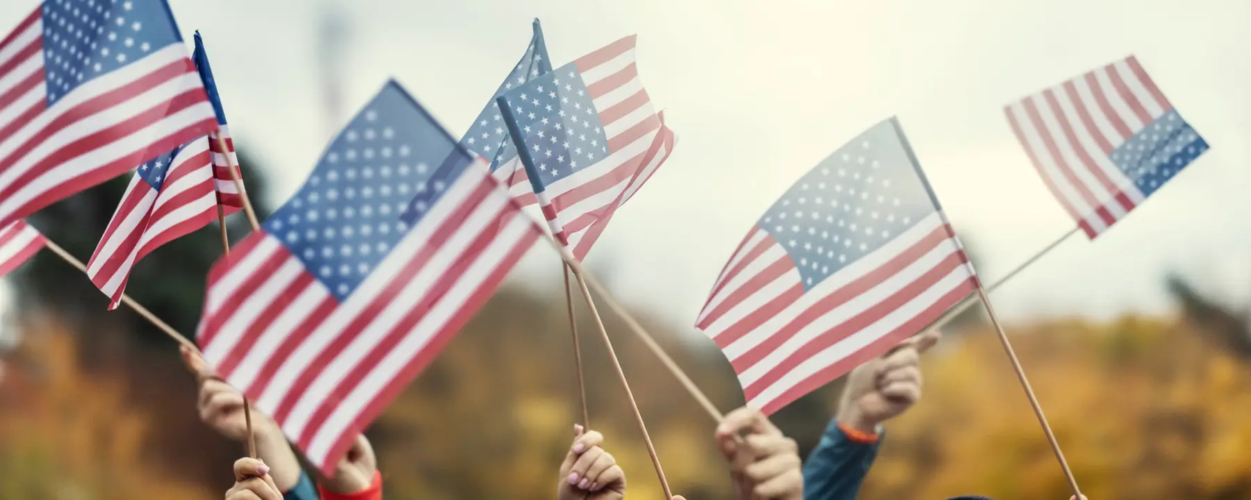 A closeup of hands waving small American flags on a fall day.