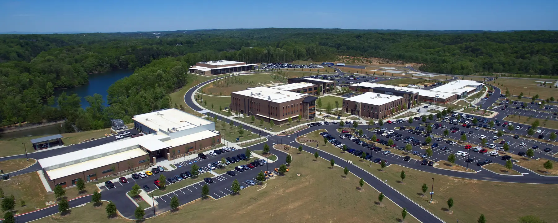Aerial view of a school campus with buildings, parking lots, and green landscape under blue skies.
