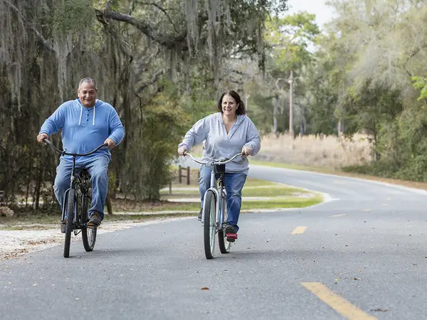 A middle-aged couple riding bikes along a tree-lined road in rural Florida.