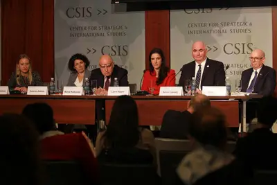 Panelists discuss topics at a conference, seated at a table in a formal setting.
