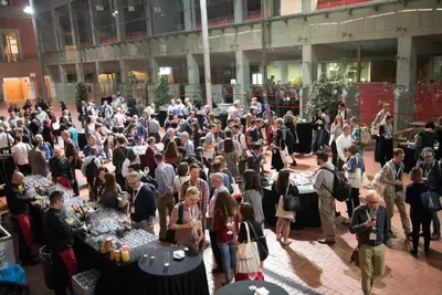 A large crowd mingles at tables, enjoying beverages in a spacious indoor venue.