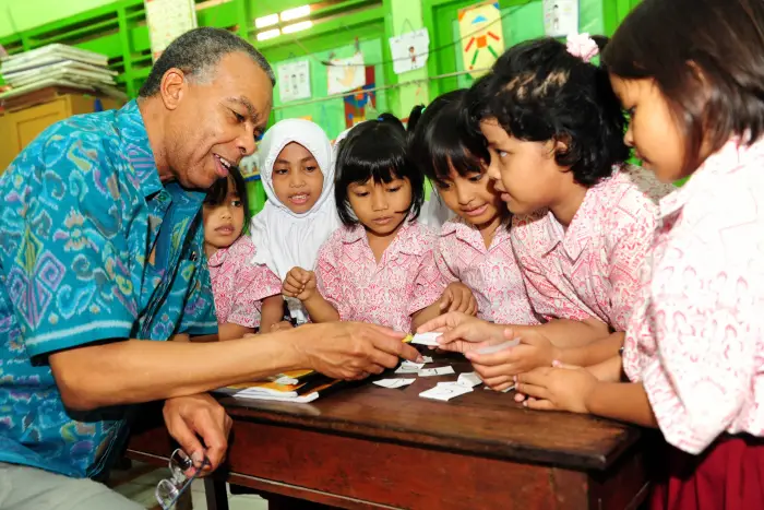 A teacher engages with young students at a table in a colorful classroom environment.