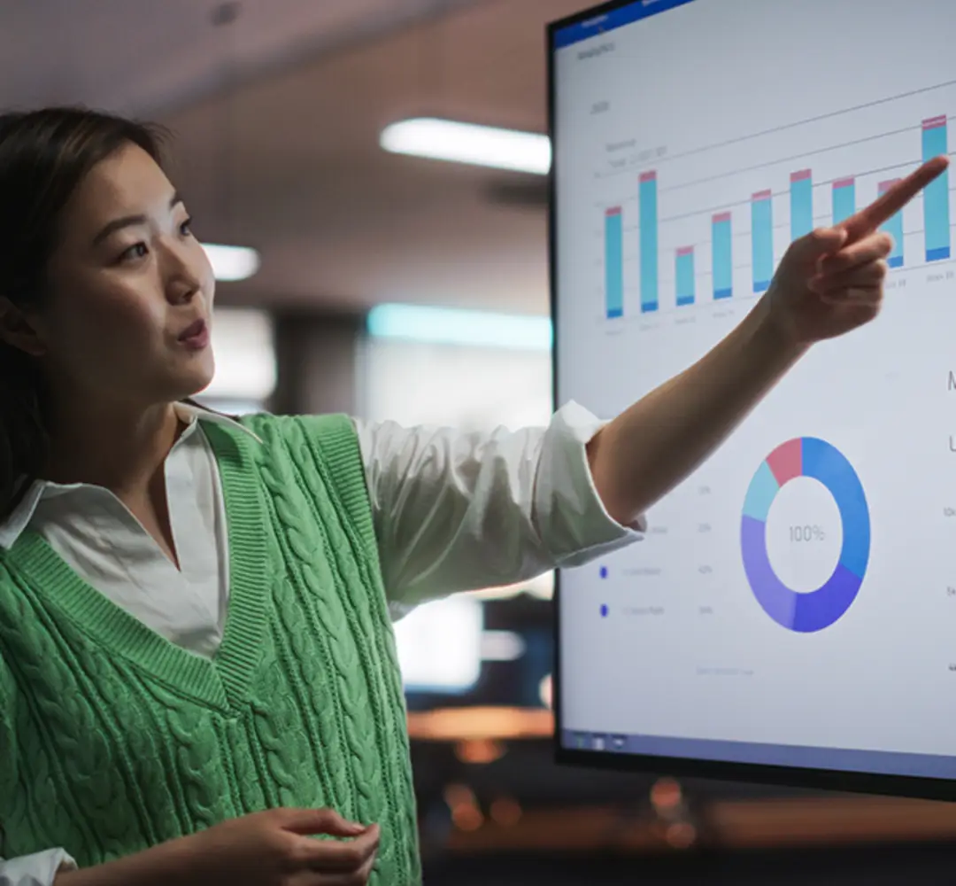 A woman points out graphs on a large monitor.