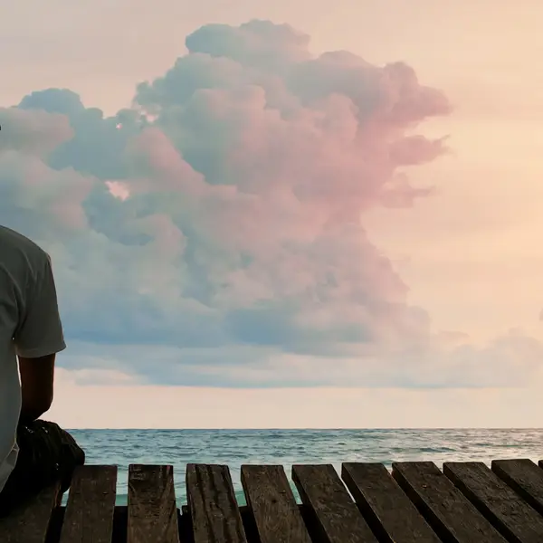 A solitary man watches the sun rise over the ocean from a pier.