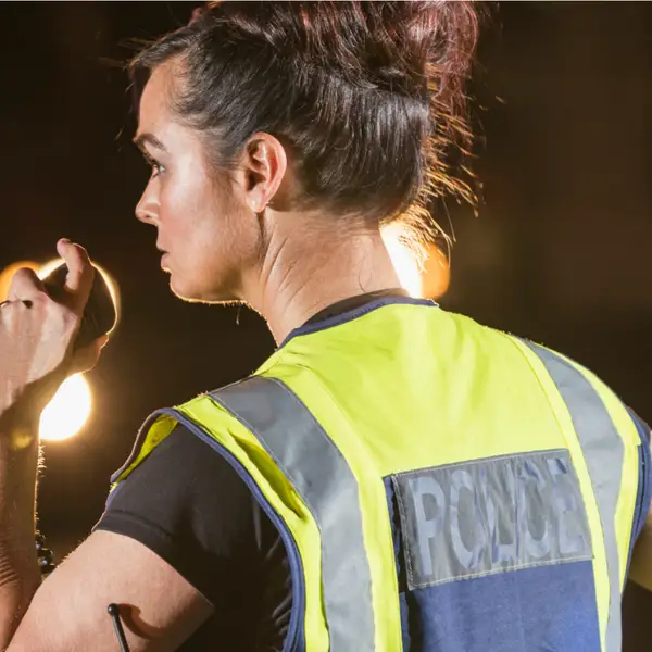 A female police officer talks into a handheld radio while watching traffic on a street at night.