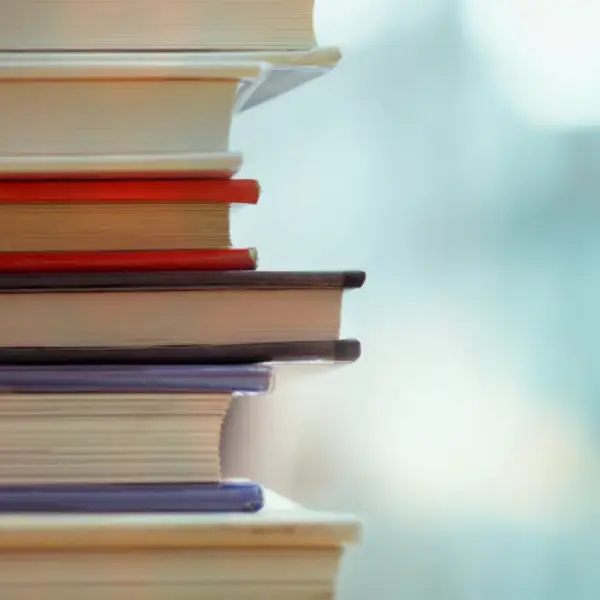 A stack of books rests vertically, showcasing colorful spines against a blurred background.