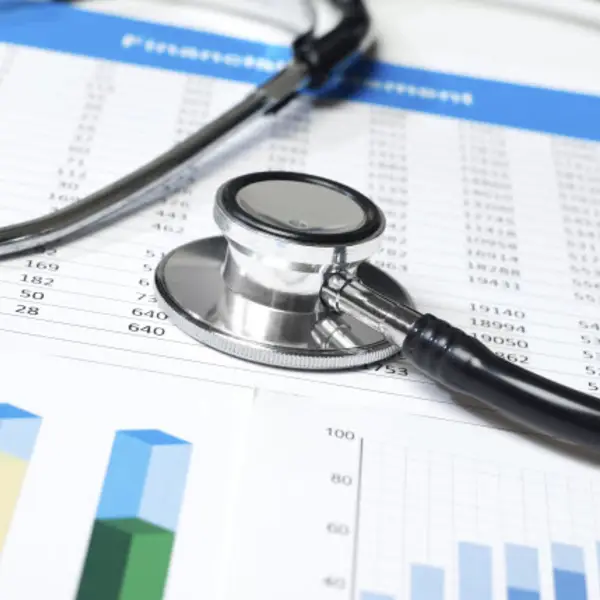 Stethoscope resting on financial documents with charts and graphs in a medical setting.