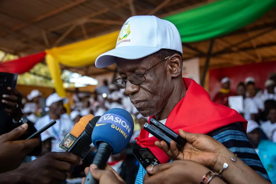 Photo of an unsmiling man surrounded by press with microphones