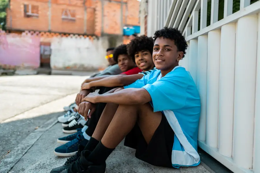 Photo of teenage boys of color smiling while sitting on the street