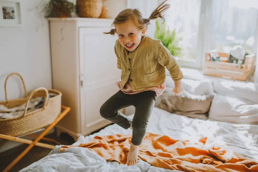 Photo of a girl smiling and jumping on a bed