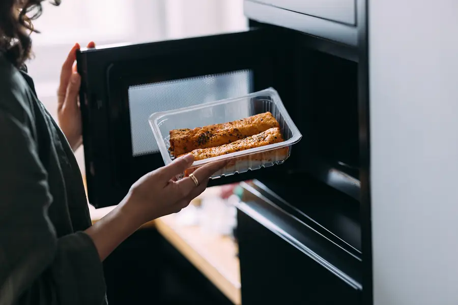 A woman places a plastic tray of food in a microwave.