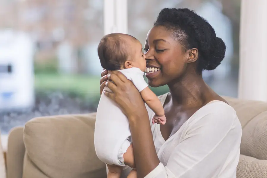 Photo of a young Black mother smiling holding her baby 