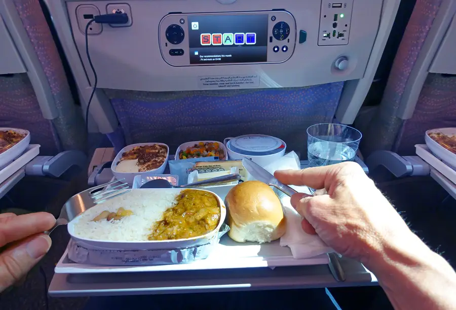 An airline passenger eats a packaged meal that has been set up on a tray table.