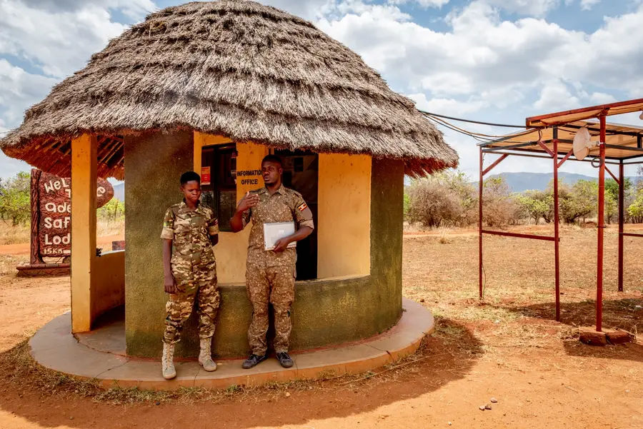 Photo of two uniformed people standing outside a hut in Uganda