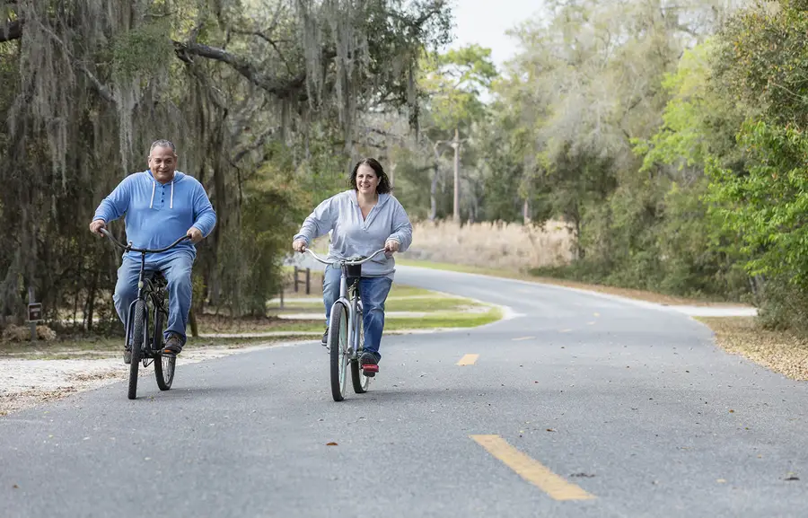 A middle-aged couple riding bikes along a tree-lined road in rural Florida.