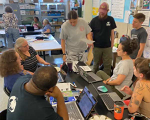 People gathering around a table with laptops in a classroom