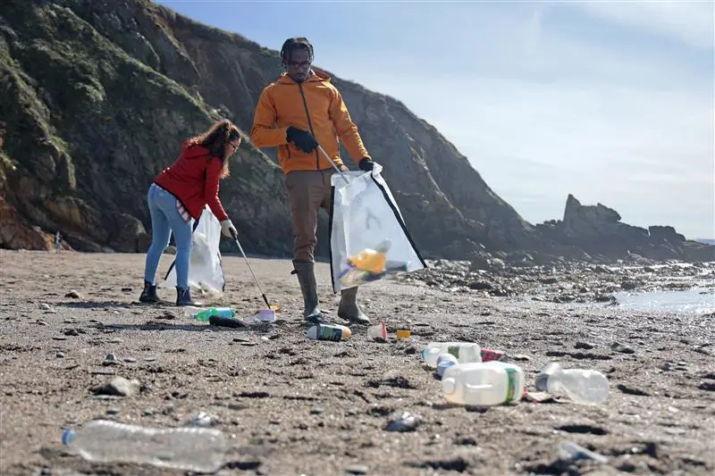 A man and woman picking up plastic bottles on the beach