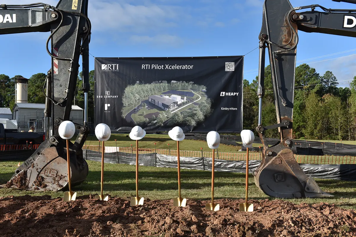 five construction hard hats on top of five golden shovels. Two cranes in the background