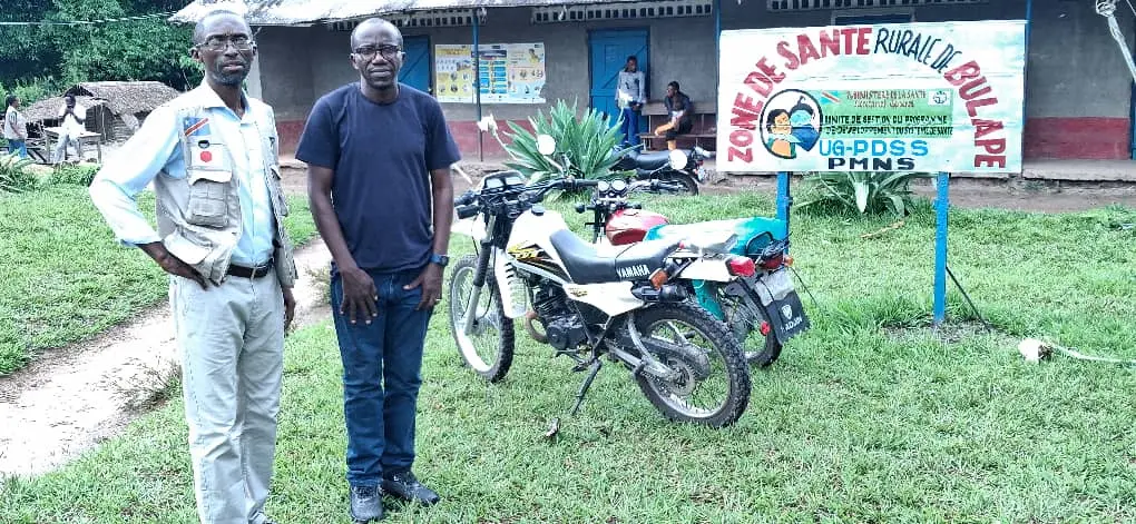 Two man standing in front of dirt bikes near a building