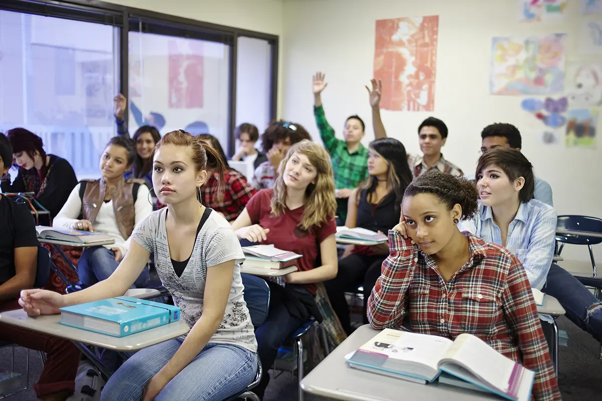 High school students raise their hands to participate in class.