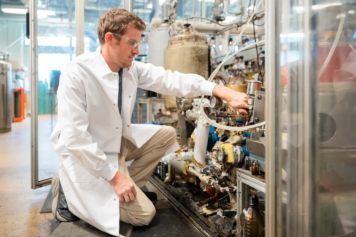 man in lab coat turning knob on industrial equipment