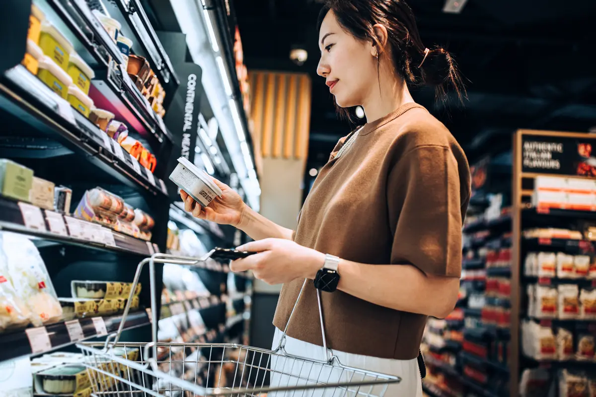 A woman inspects a label while shopping at a grocery store.