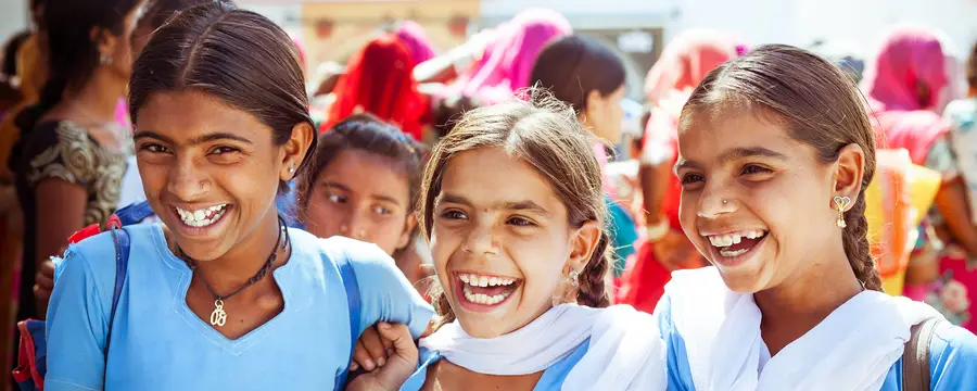 Three girls in India wearing matching light blue outfits and smiling for the camera.