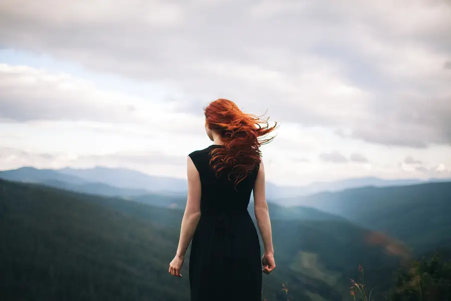 A woman walks along a misty mountain ridge.