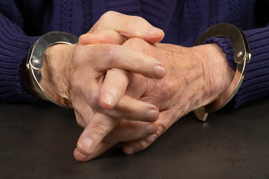 A closeup photo of a senior man's hands in handcuffs.