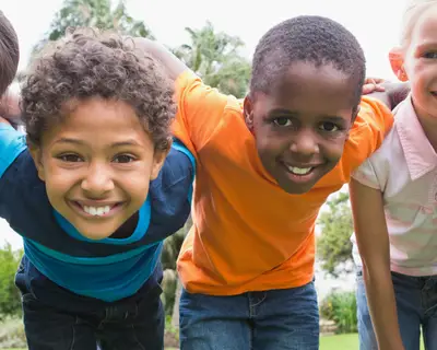 A diverse group of children link arms while playing outside.