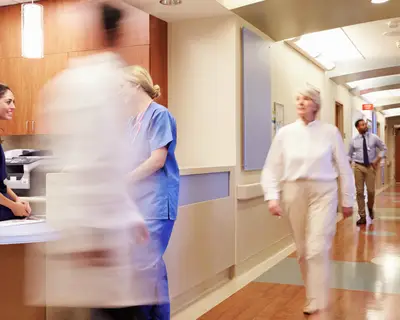 Doctors and nurses walk in a busy hospital hallway.
