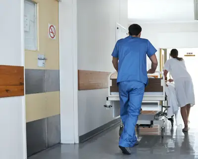 Two health care workers transport a patient through a hospital hallway on gurney