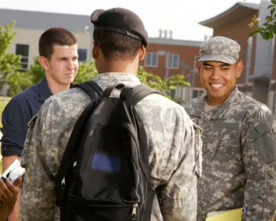 Two students in military uniforms talk with other students on a college campus.