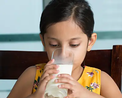 A young girl drinks a glass of skim milk