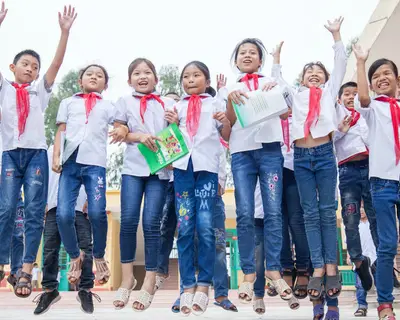 Schoolchildren in Vietnam hold hands, smile, and jump.