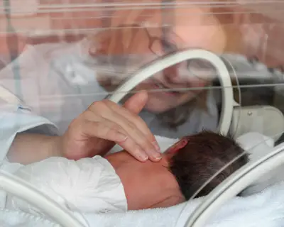 A woman touches a premature baby in an incubator
