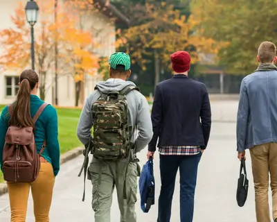 A group of students walks along a tree-lined path, surrounded by autumn-colored foliage.