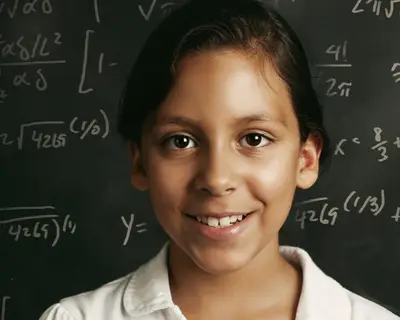 A young student in front of a chalkboard with equations written on it