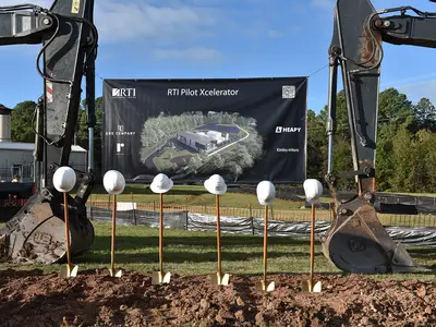 five construction hard hats on top of five golden shovels. Two cranes in the background