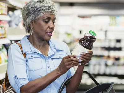 A woman checks the label on a bottle of juice in a grocery store.