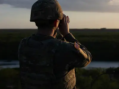Military personnel looks through binoculars
