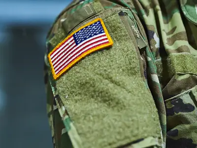 A closeup of a U.S. soldier in camouflage clothing with an American flag patch on the shoulder.