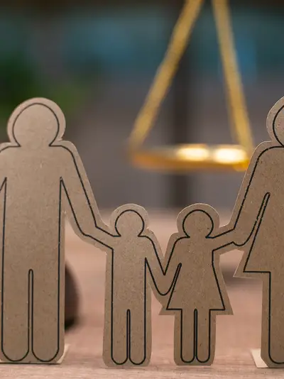 Paper cutouts representing a family stand in front of a judge's gavel and a set of scales.