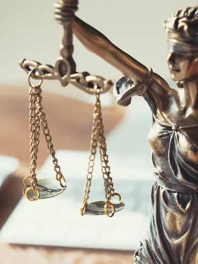 A small bronze sculpture of blindfolded Lady Justice stands on a desk with a computer and mouse.