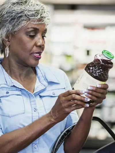 A woman checks the label on a bottle of juice in a grocery store.