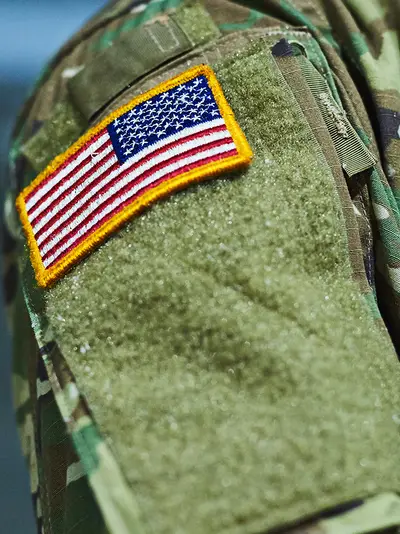 A closeup of a U.S. soldier in camouflage clothing with an American flag patch on the shoulder.