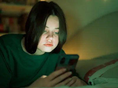 Photo of a young teenager in her room in the dark looking at her phone