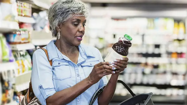 A woman checks the label on a bottle of juice in a grocery store.