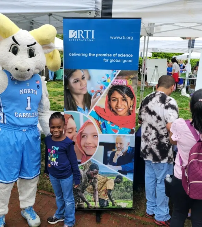 Photo of a child and the UNC mascot in front of an RTI banner at the UNC Science Expo